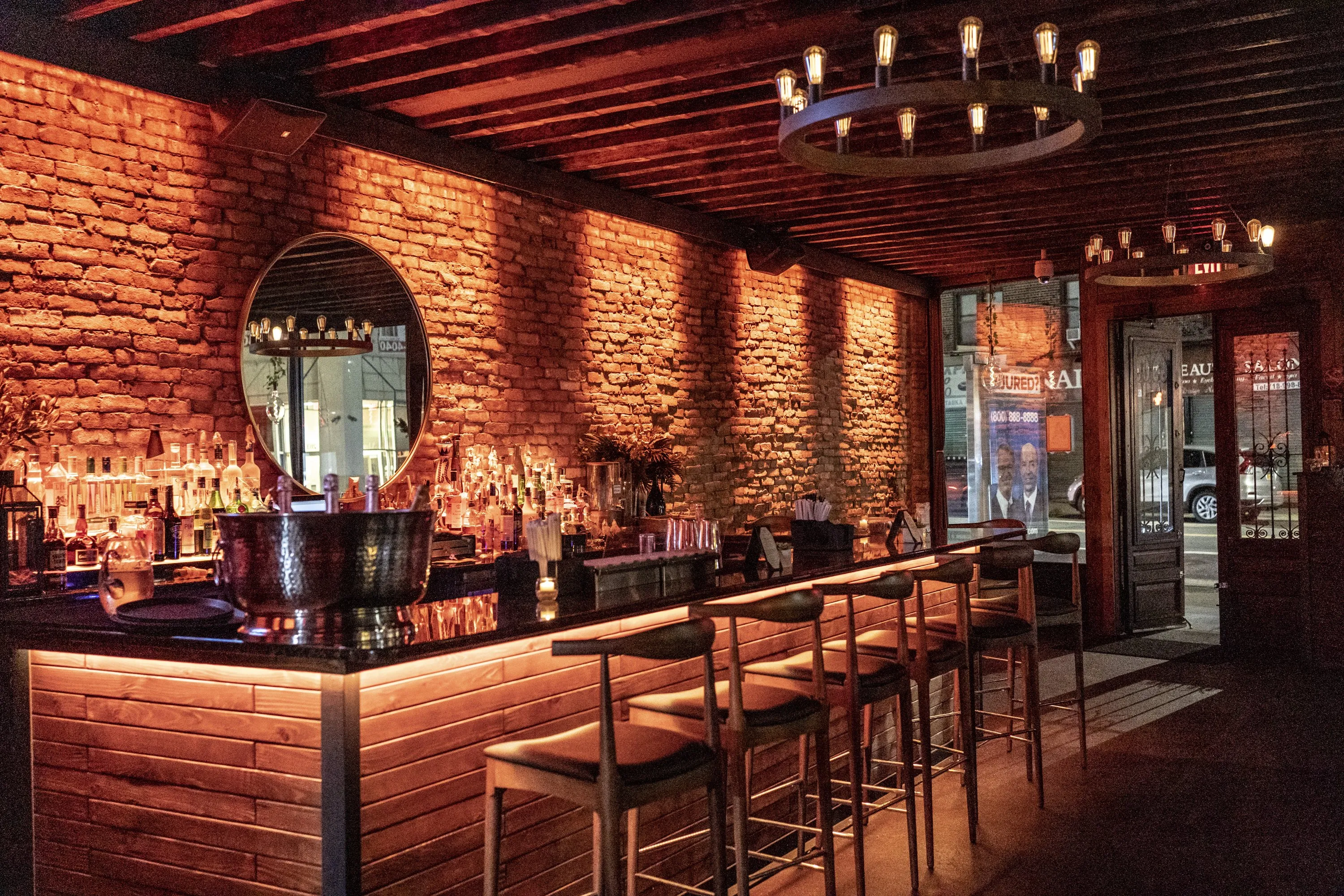 The bar at Mera: exposed brick, candle chandeliers and a row of bar stools under warm light.