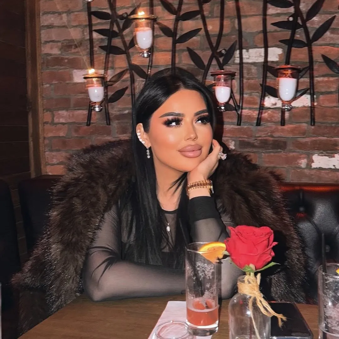 A guest at a booth with a cocktail and a single red rose, iron vine sconces on the brick wall.
