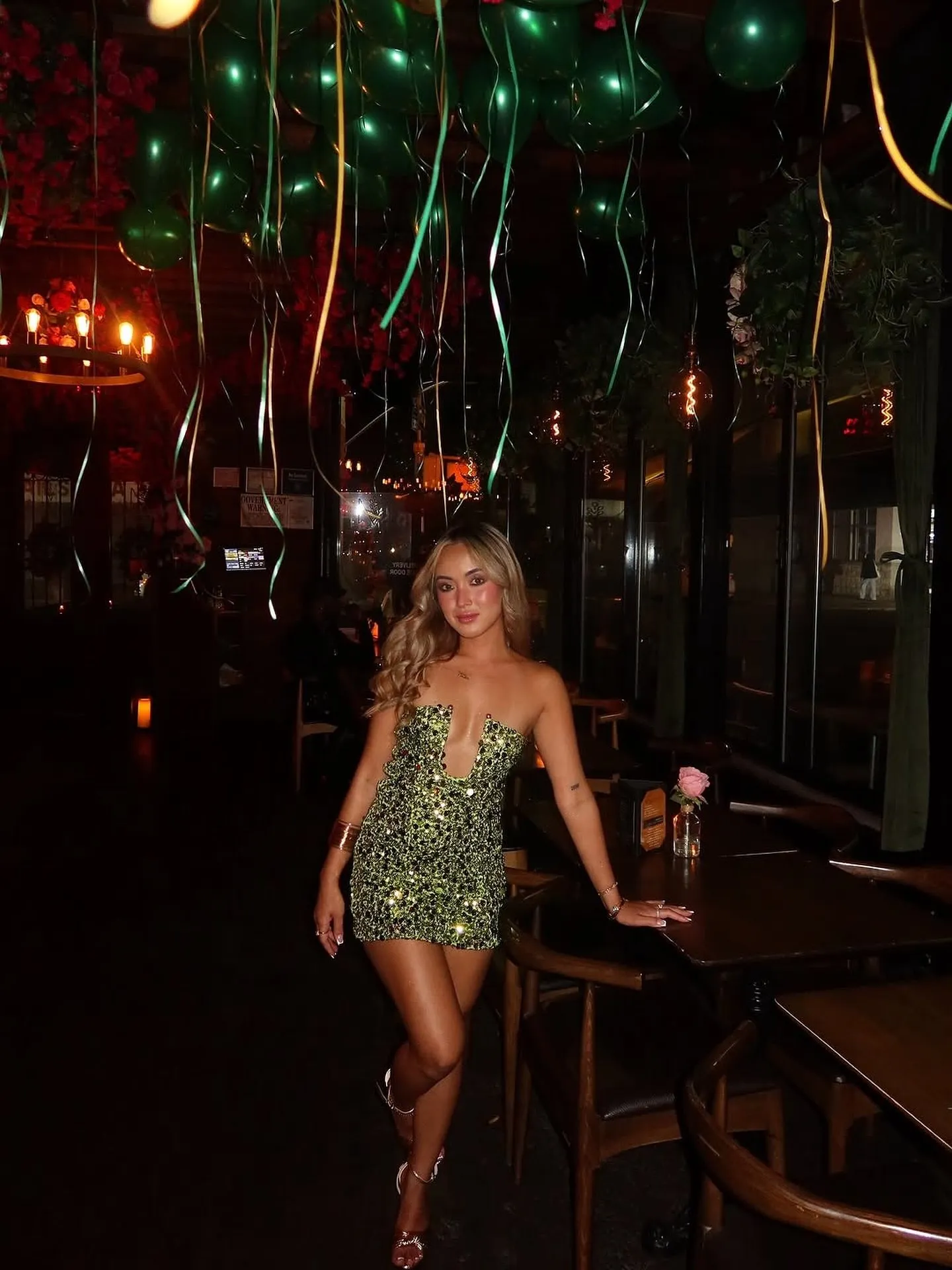A guest in a green sequined dress in the dining room under hanging green lights.