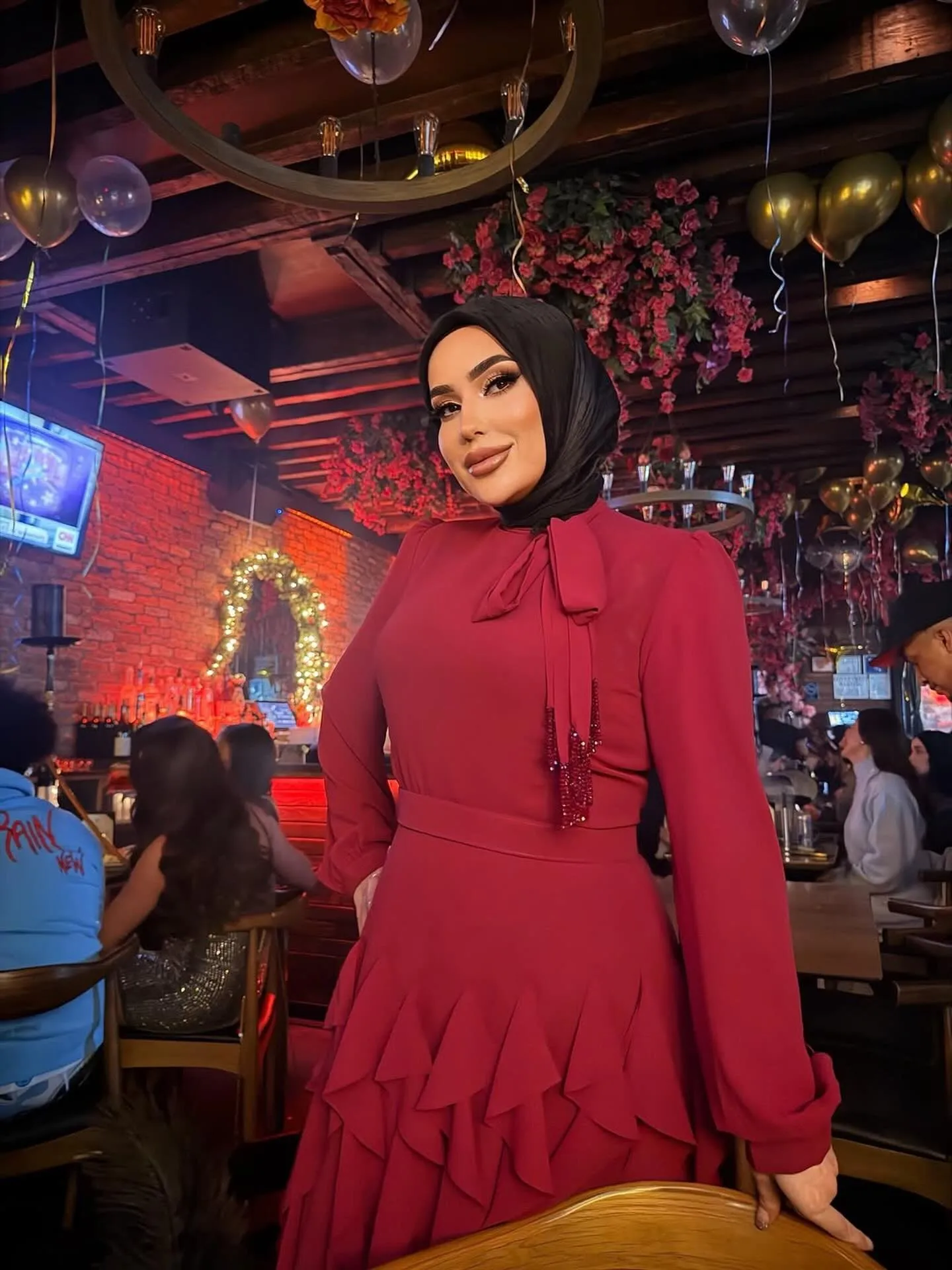 A guest in a red dress in the dining room, balloons and flowers overhead.