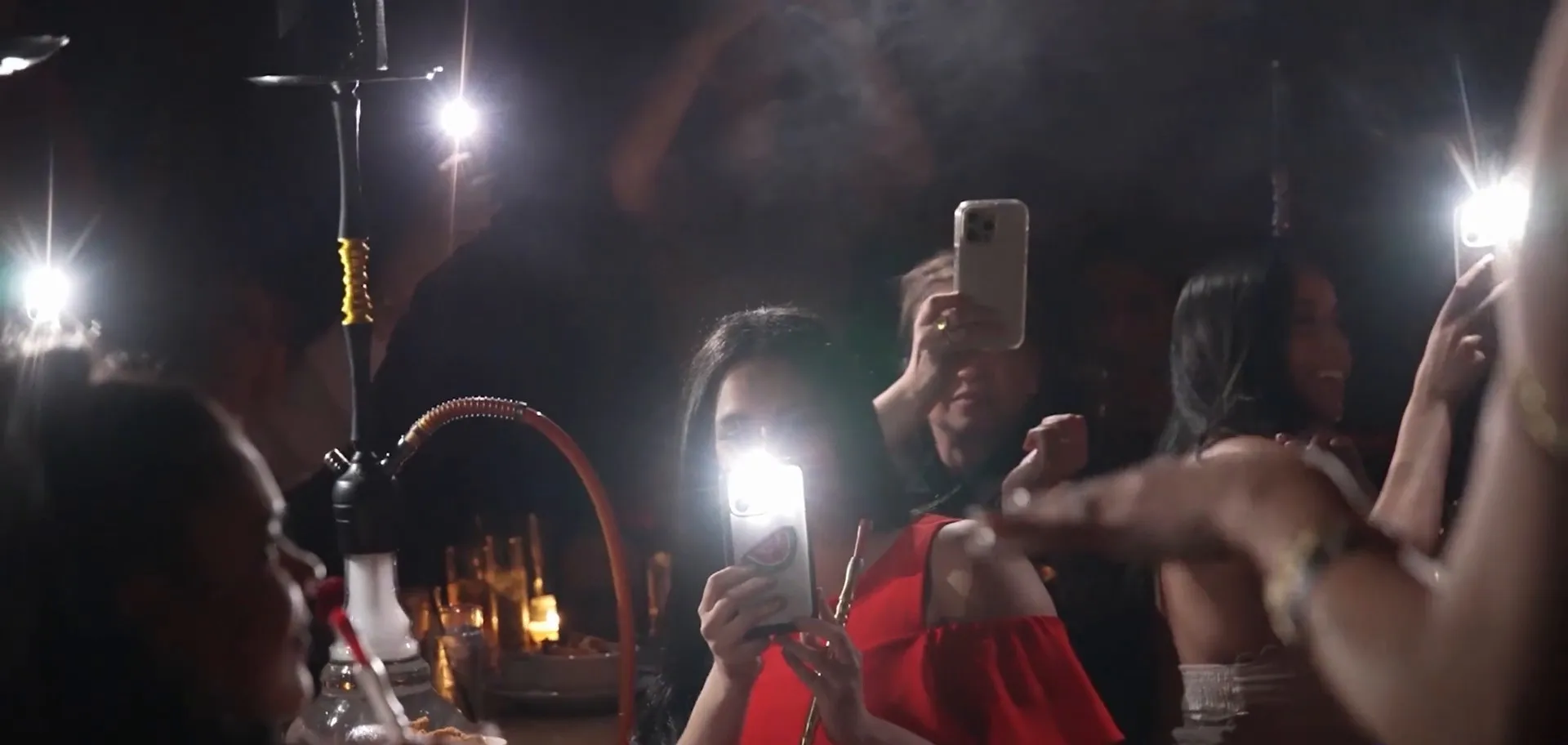 A weekend night at Mera: a hookah on the table at left, guests holding up their phone lights in the lounge.