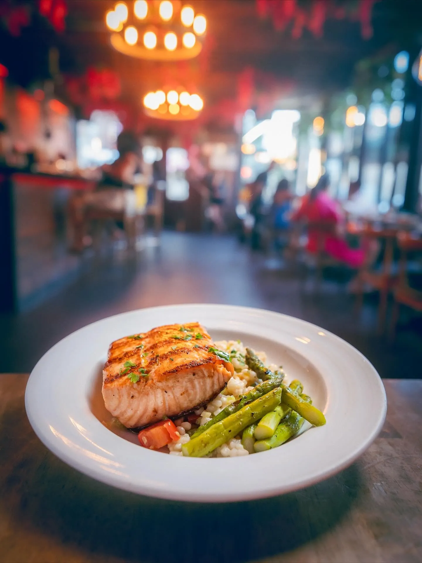 Grilled salmon with asparagus on a white plate, the dining room glowing behind it.