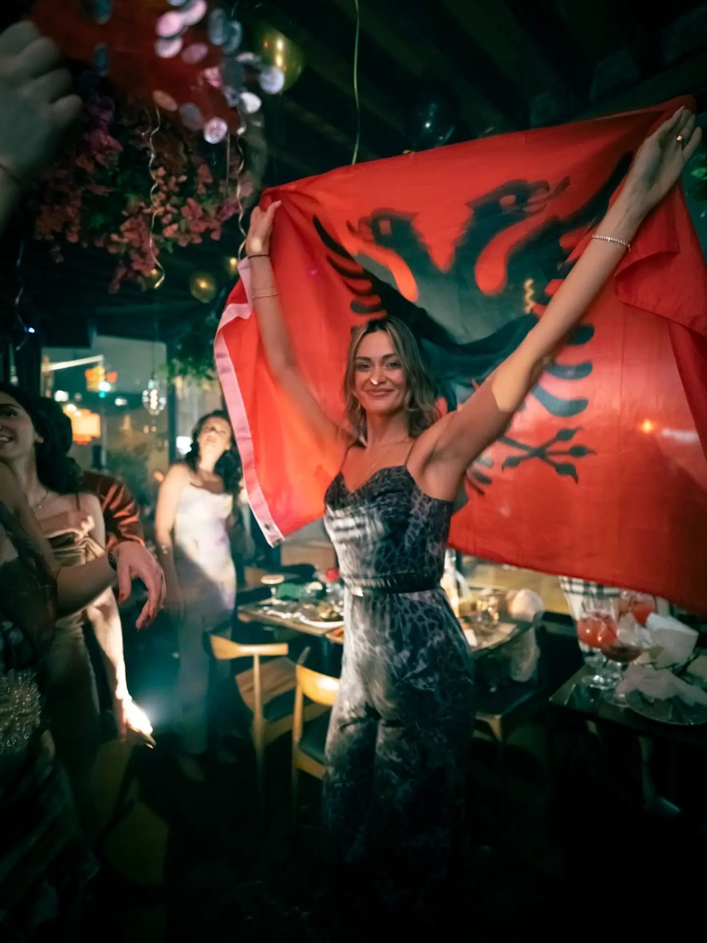 A guest waving a red Albanian flag above a busy late-night crowd.